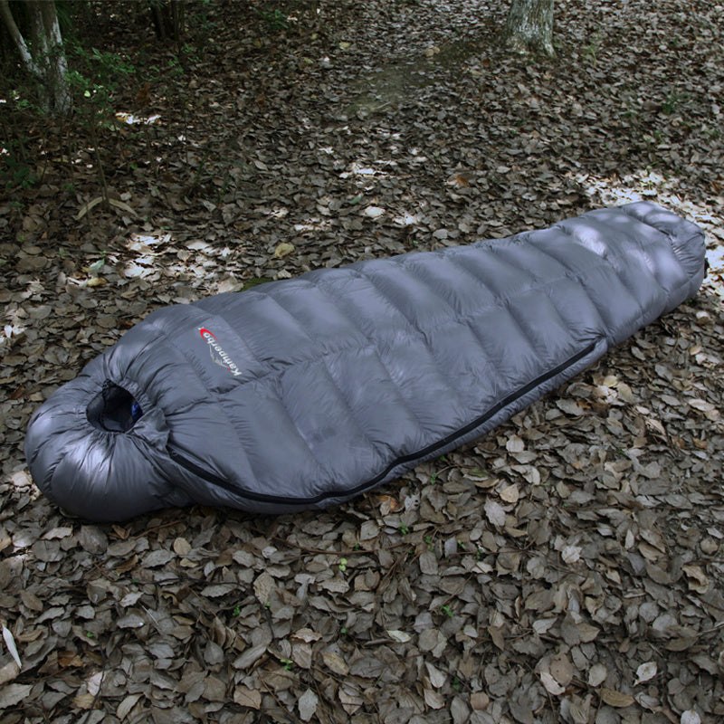 Goose down sleeping bag with compression sack on forest ground, perfect for winter camping.