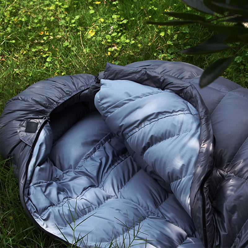 Goose down sleeping bag with compression sack on grass, showcasing its warmth and comfort for winter camping.