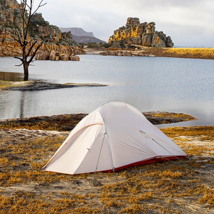 Portable rain proof tent by a lakeside with scenic rocky landscape