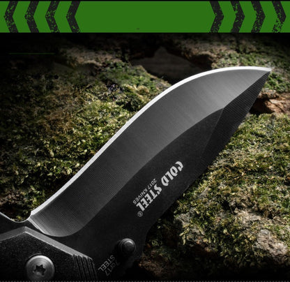 Close-up of 7Cr17 Stainless Steel Folding Knife blade with Cold Steel engraving, displayed on a forest floor.