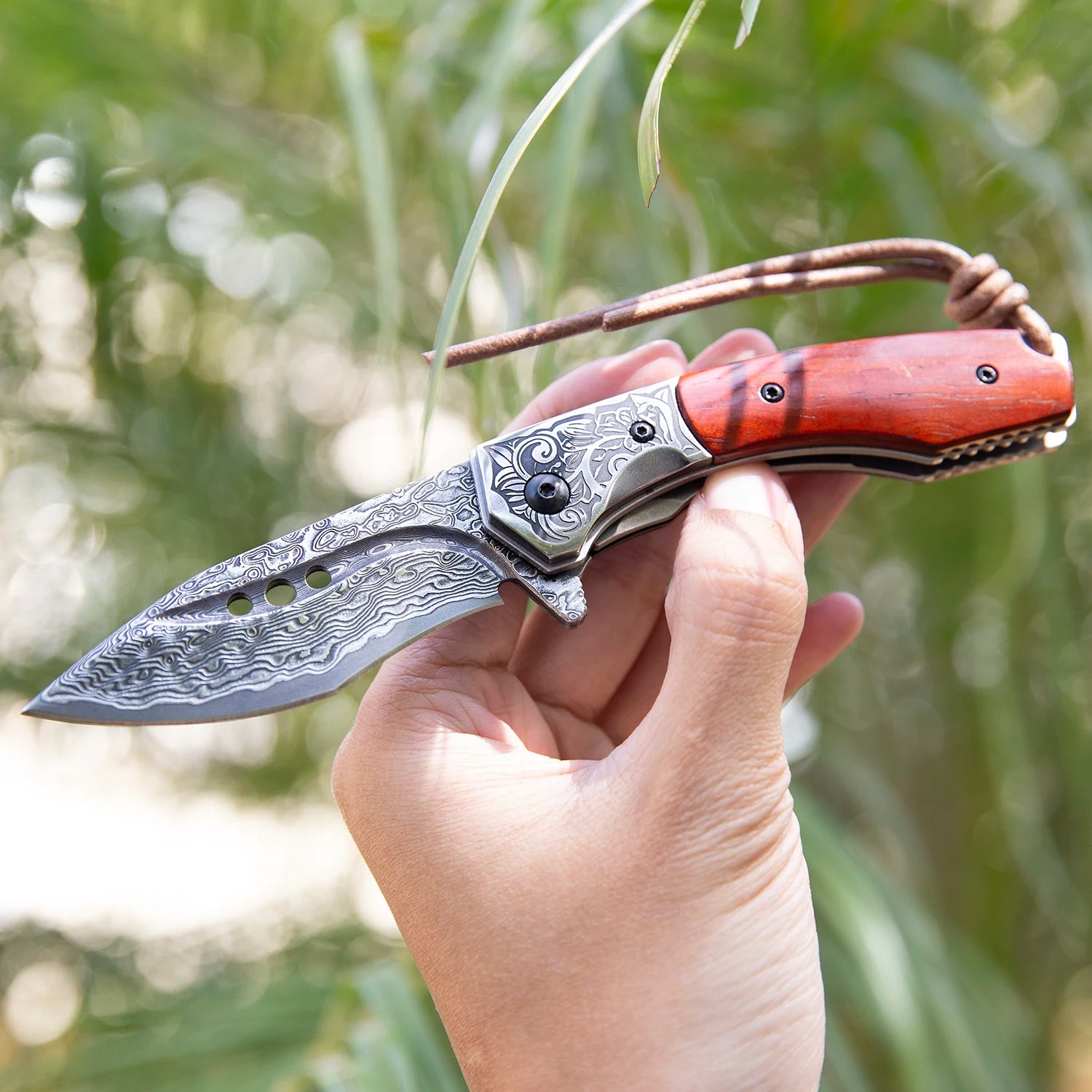 Damascus steel knife with rosewood handle held outdoors