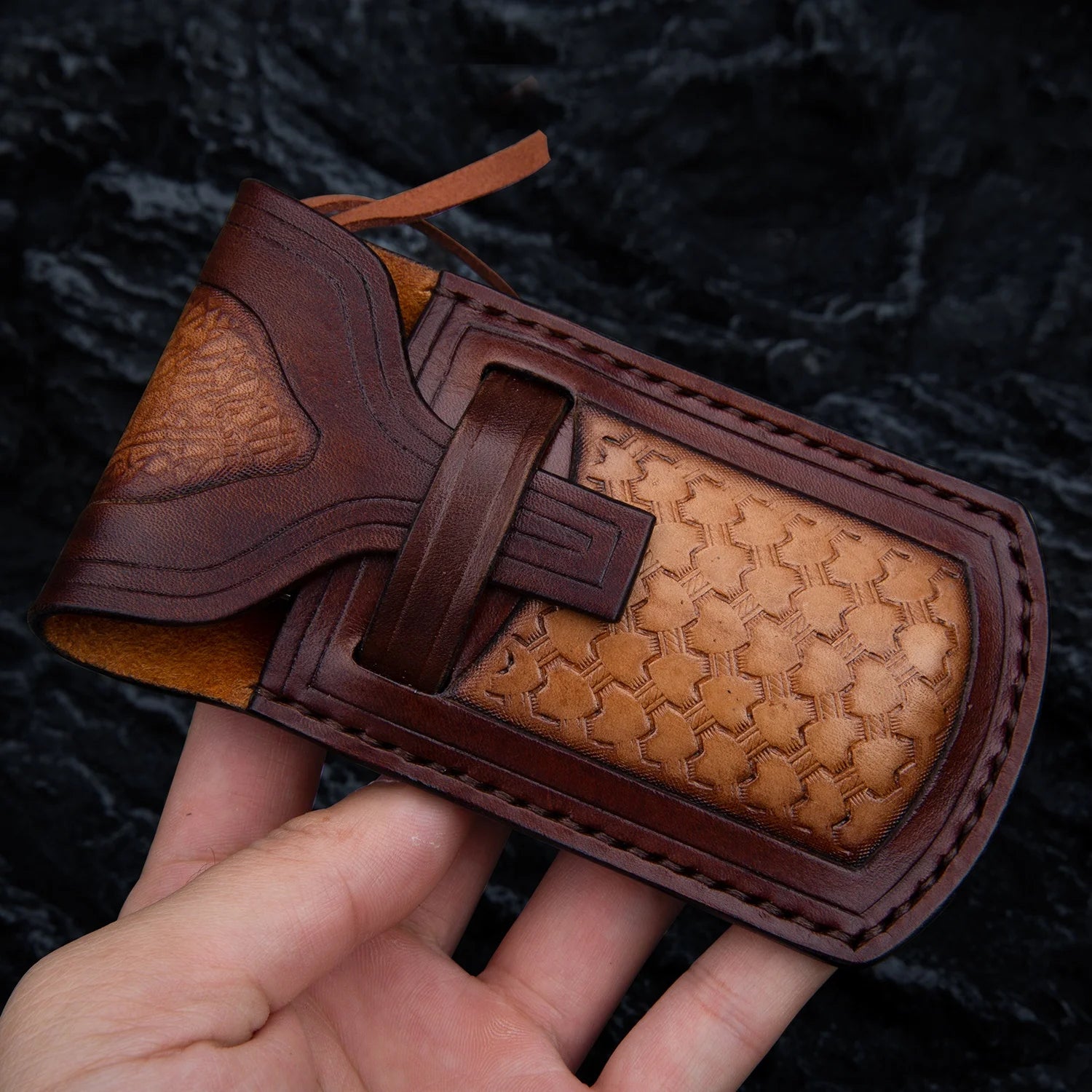 Leather sheath for handmade Damascus Steel Knife with intricate design held in hand.