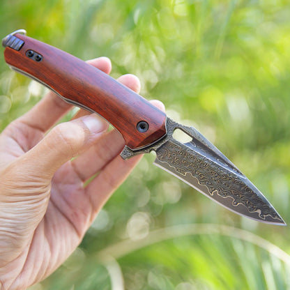 Damascus steel knife with rosewood handle being held outdoors.