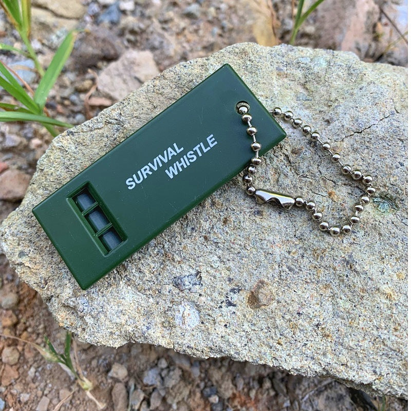 High Decibel Survival Whistle with 3-Frequency Settings in Dark Green on a Rock, Essential for Outdoor Camping and Hiking