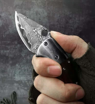 Hand holding a Mini Damascus Steel Folding Knife with CNC water-ground blade and red sandalwood handle