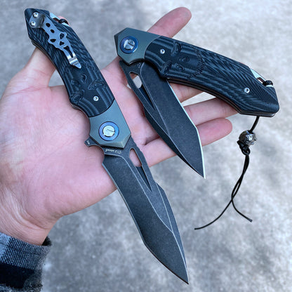 Hand holding two D2 steel survival folding knives with G10 handles and titanium alloy washers