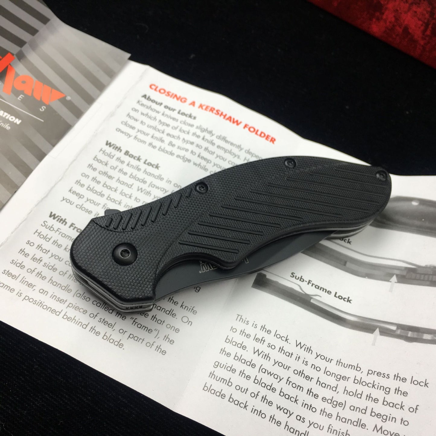 Black survival folding knife with ABS handle resting on user manual.