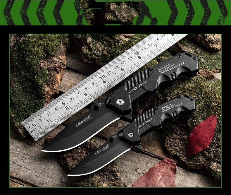 7Cr17 Mov stainless steel folding knives with black aluminum alloy handles placed beside a ruler on a wooden surface with moss and leaves.